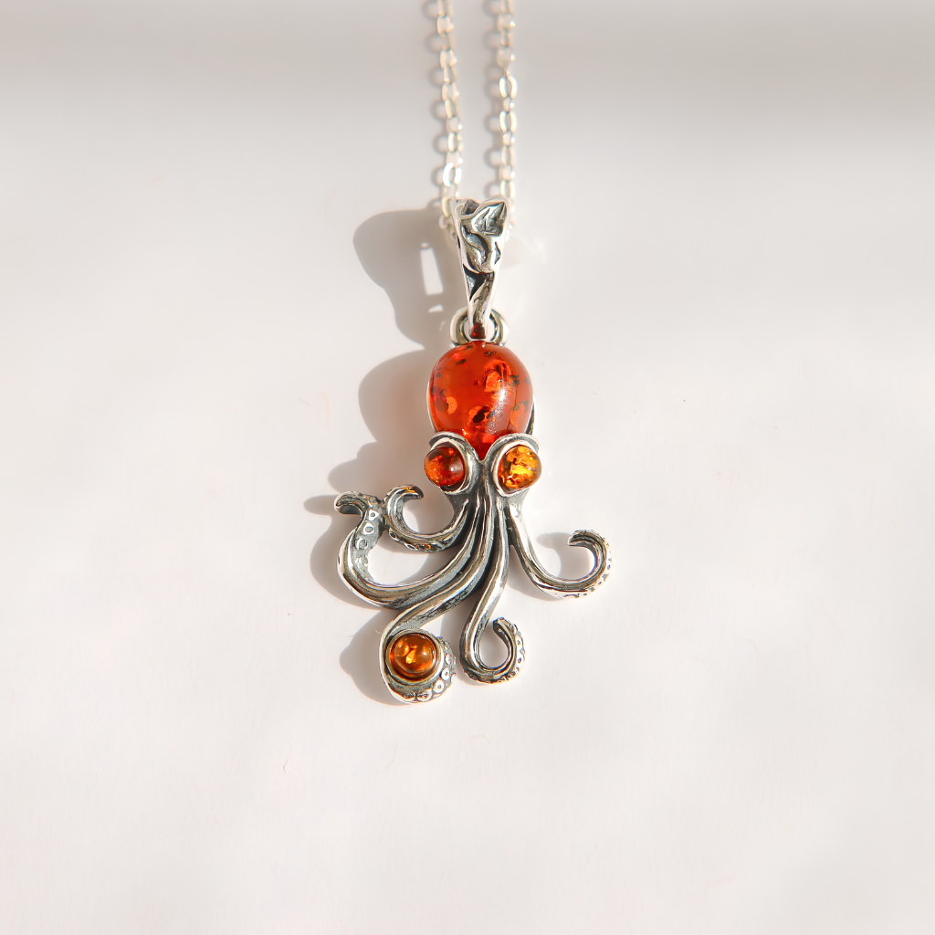 A silver amber octopus pendant necklace with amber-colored gemstones, shown on a plain white background with a soft shadow.