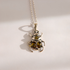 A silver amber beetle necklace with two oval amber-colored gemstones on the front and a smaller round amber stone above, hanging from a silver ball chain on a light background.