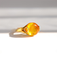 A gold ring with a large, polished Baltic amber-colored cabachon gemstone, photographed on a clean white surface with soft shadows.