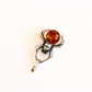 A silver amber spider pendant with four black eyes and a orange amber gemstone shown on a plain light gray background.
