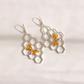 A pair of silver-toned drop bee earrings featuring a hexagonal honeycomb pattern with small amber-orange and silver butterfly details, displayed on a clean white background.