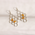 A pair of silver-toned drop bee earrings featuring a hexagonal honeycomb pattern with small amber-orange and silver butterfly details, displayed on a clean white background.