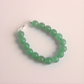 Green beaded jade bracelet on a light pink background
