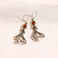 A pair of silver-toned amber octopus dangle earrings with polished amber-orange gemstones, displayed on a clean, light beige background.