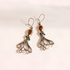 A pair of silver-toned amber octopus dangle earrings with polished amber-orange gemstones, displayed on a clean, light beige background.
