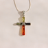 A silver amber cross pendant necklace featuring three vertical bars of amber in yellow-green, black, and orange-red, with a embellished center, suspended from a thin silver chain against a plain light background.
