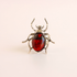 A scarab ring featuring a polished dark red oval cabochon stone set in textured silver-tone metal, shown on a plain light background.