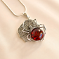 Spider amber necklace with red gem and silver web design on a beige background