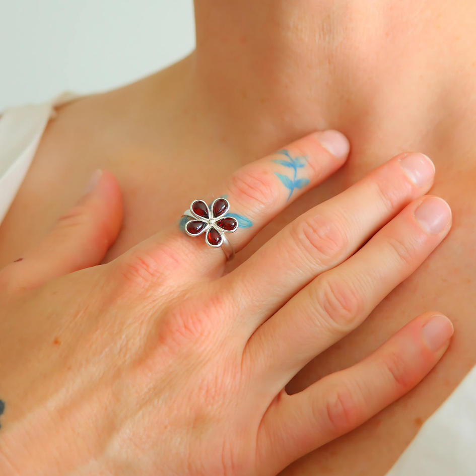 Close-up of a hand wearing a floral ring with blue accents on a light background