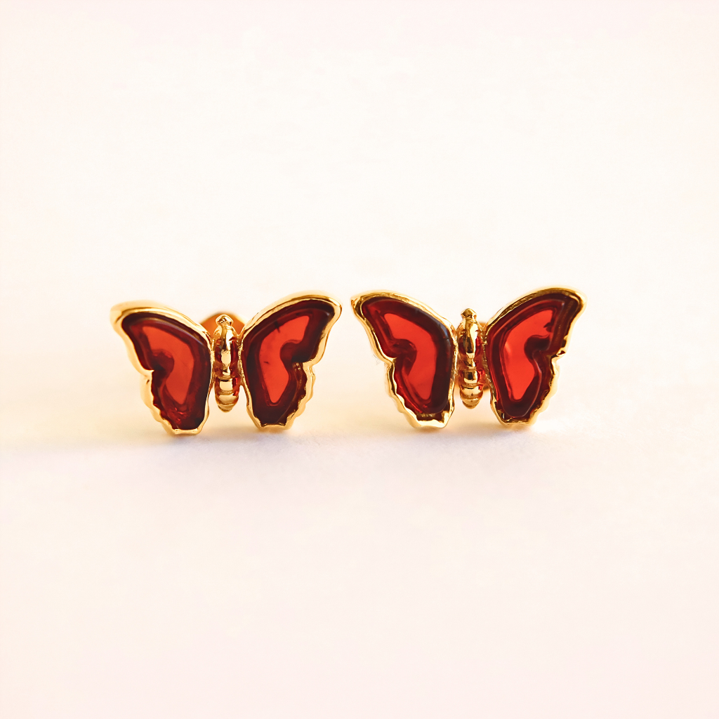 Butterfly-shaped gold stud earrings with red wings and gold frames on a white background