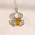 A baltic amber silver spider pendant necklace with a carved orange amber belly and a small orange gem on its back, shown on a plain light background.