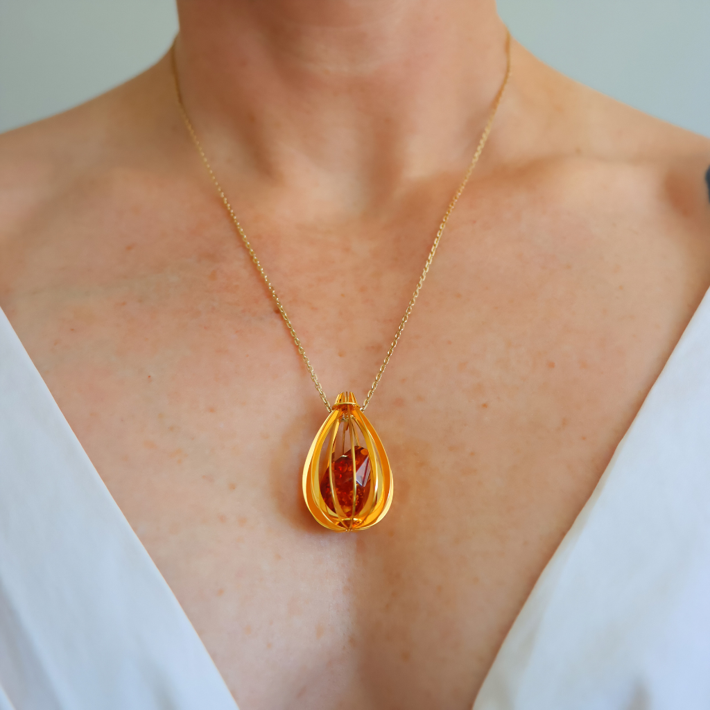 Gold amber necklace with a teardrop-shaped amber pendant on a person wearing a white top.