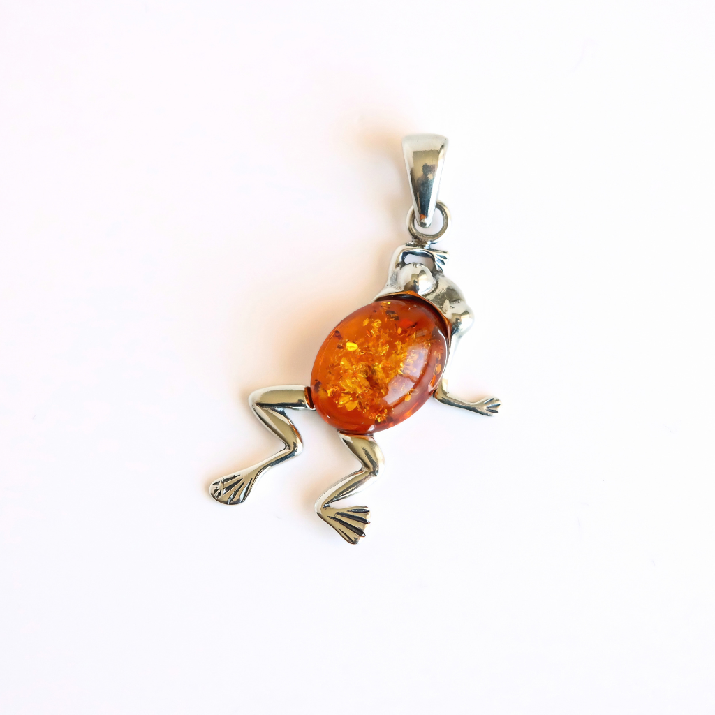 A frog pendant necklace featuring a polished amber-colored oval body and silver-toned metal limbs and bail, photographed on a plain white background.