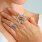 Silver sun ring with a red stone on a person's finger against a light background