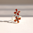 A Baltic amber flower ring  in sterling silver featuring two small flower motifs with amber-colored petal inlays, photographed on a light beige surface with soft shadows.