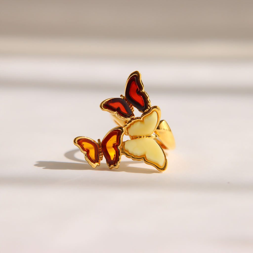 Af gold amber butterfly ring with red and yellow amber details, displayed on a clean white surface with soft shadows.