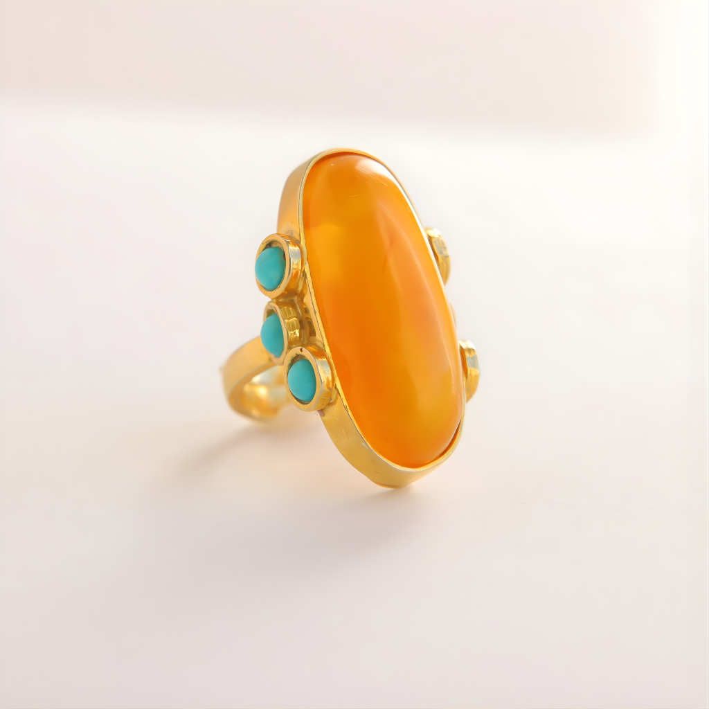 Gold amber ring with a large orange stone and smaller turquoise stones on a light background