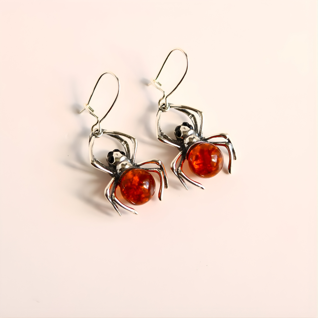 Spider-shaped sterling silver earrings with amber-colored centers on a light beige background
