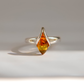 A silver amber ring featuring a marquise-cut amber gemstone, displayed on a neutral light gray background with a soft shadow.