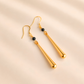 Gold drop earrings with black beads on a beige background