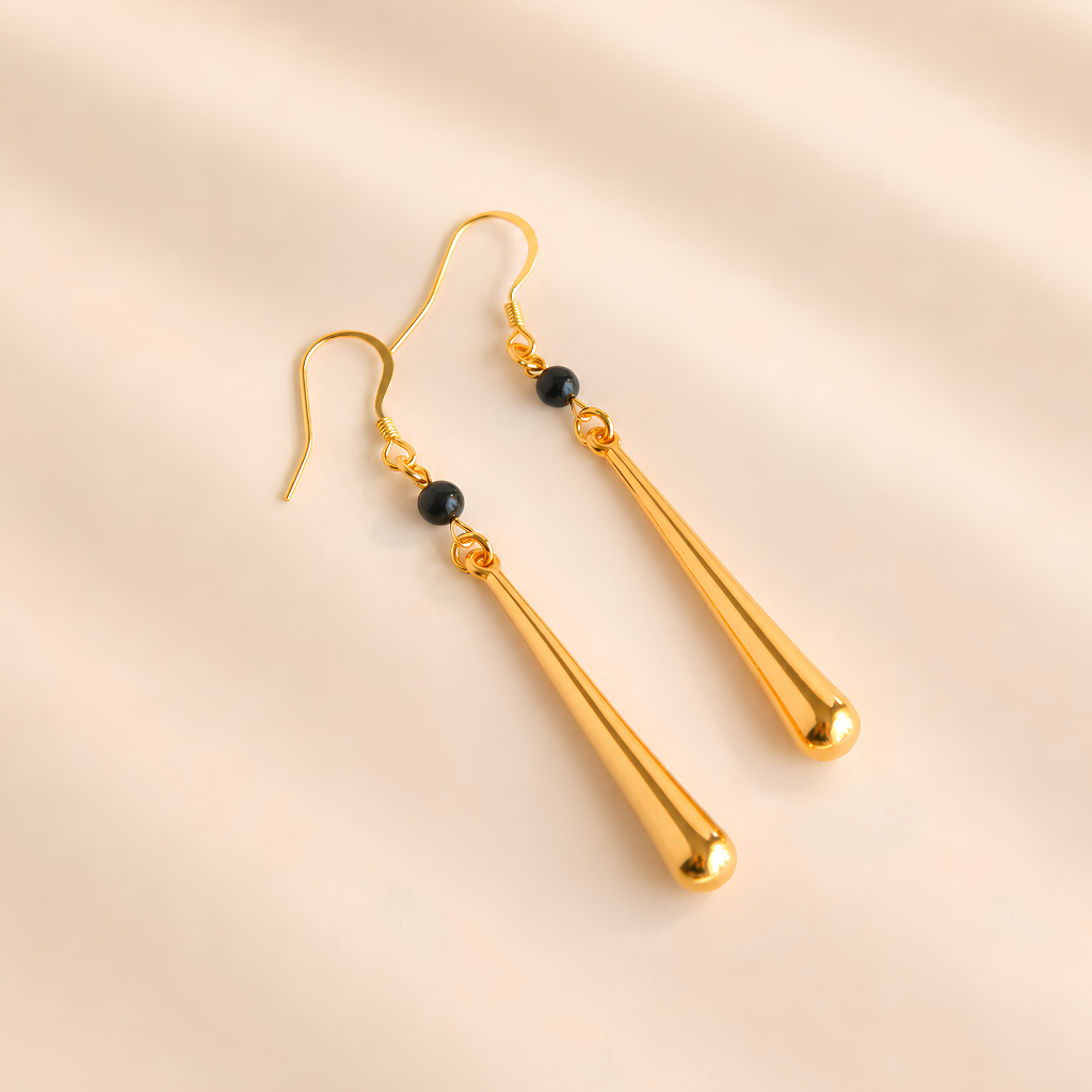Gold drop earrings with black beads on a beige background