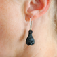Black amber bat earring worn on an ear with a blurred background