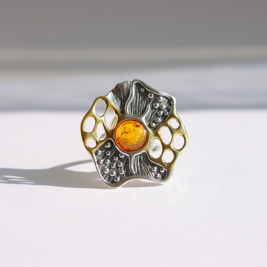 A textured silver and gold amber statement ring featuring a central amber-colored round gemstone, photographed on a clean white surface with soft shadows.
