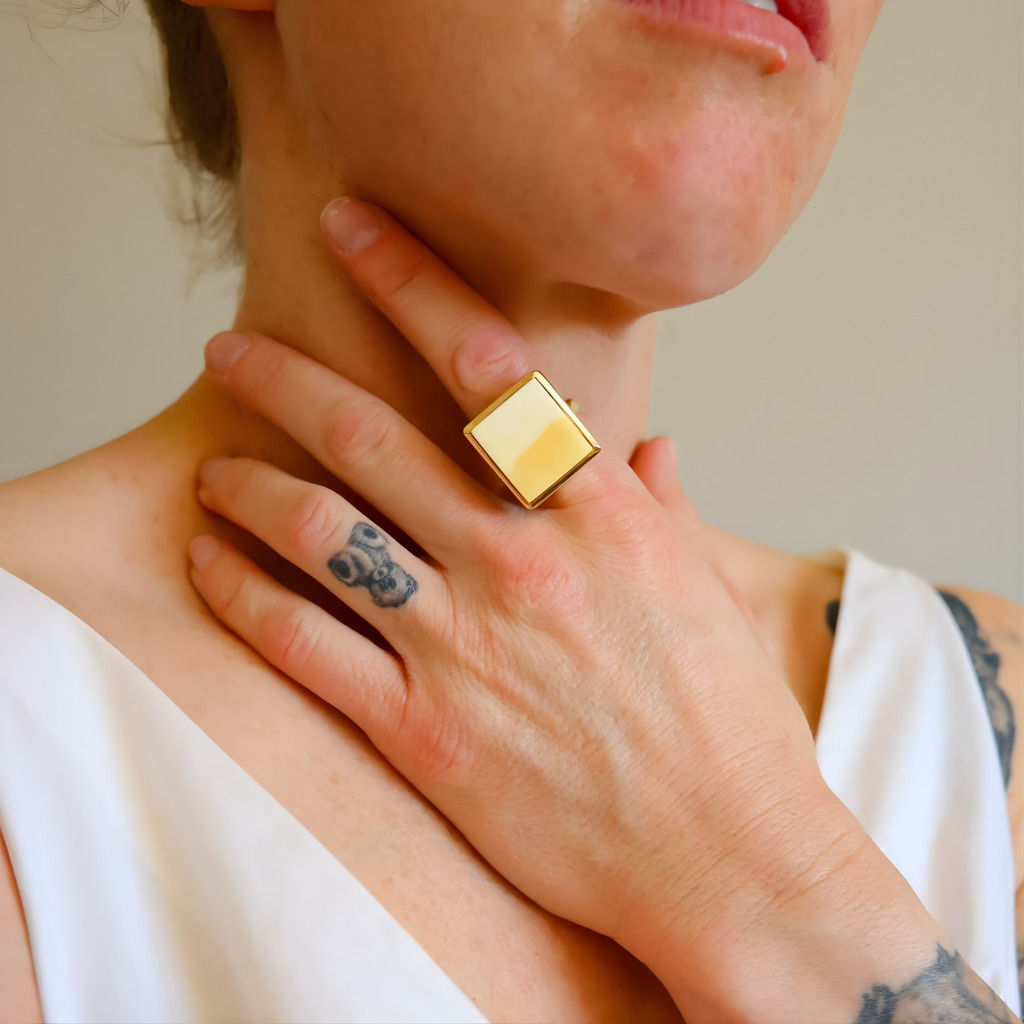Person wearing a gold amber ring on their finger, with a neutral background