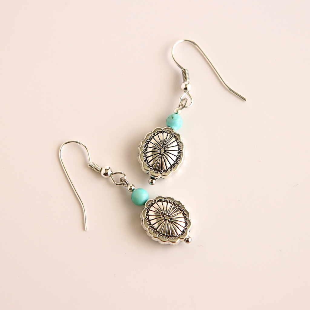 Silver western earrings with turquoise beads on a beige background