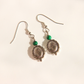 A pair of silver-toned malachite dangle earrings with green beads and circular fan-shaped charms, photographed on a plain off-white background.