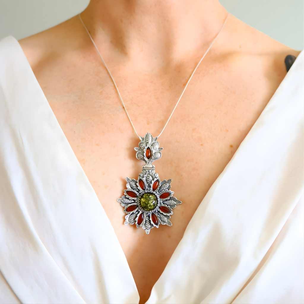 Silver necklace with a green amber floral pendant featuring green and red stones on a white background