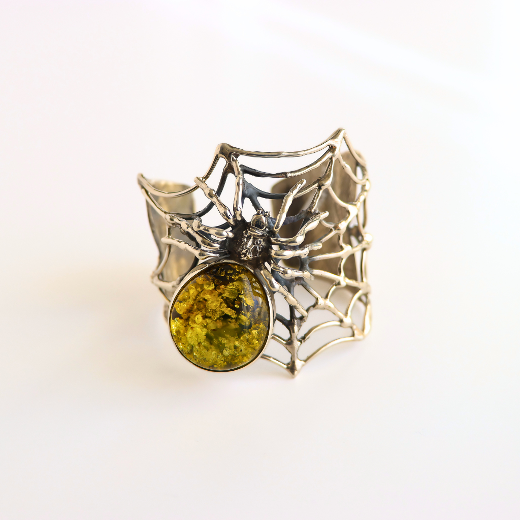 A silver spider amber bracelet with a large oval yellow-green stone, set against a plain white background.