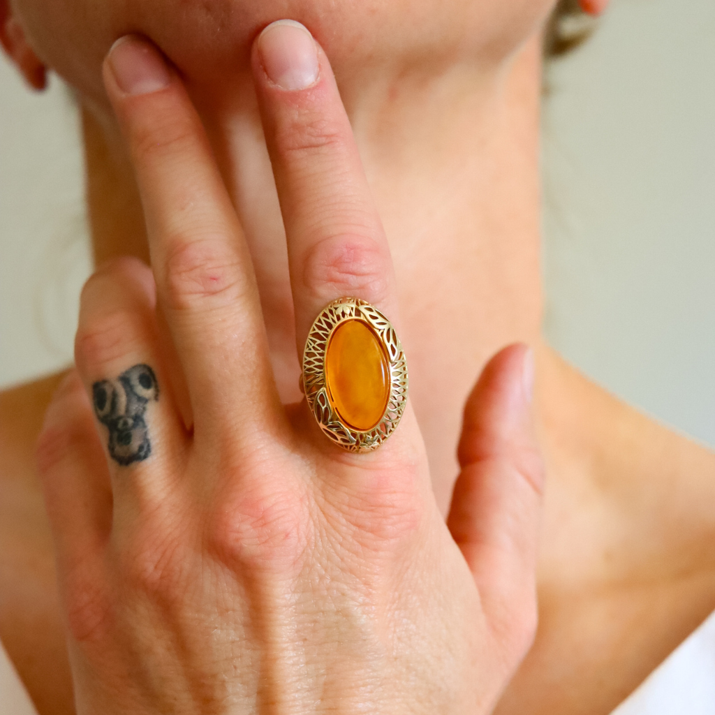 Close-up of a hand wearing a gold amber ring with an amber stone, with a blurred background.