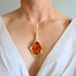 amber Necklace with a large orange pendant worn by a person in a white top.