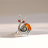 A snail-shaped ring made of sterling silver metal with a polished amber-orange shell and two small red eye stones, photographed on a clean light beige background.