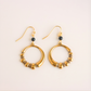Gold hoop earrings with black beads on a beige background