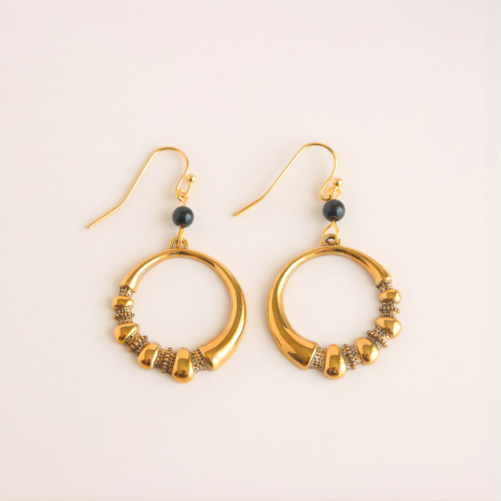 Gold hoop earrings with black beads on a beige background