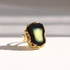 A gold amber ring featuring a large, irregular-shaped black amber stone with a yellow and white center, photographed on a white surface with soft shadows.