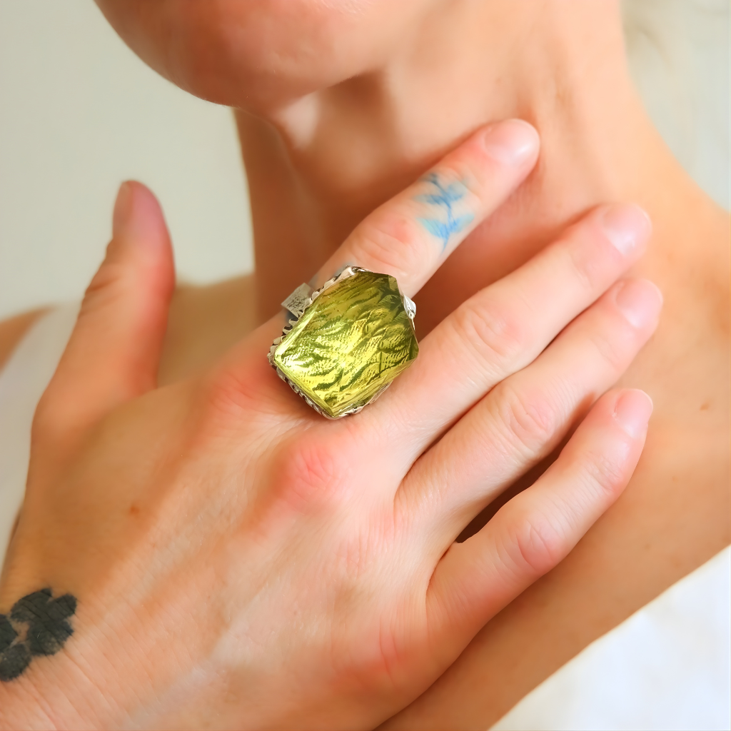 Close-up of a hand wearing a green amber ring with a textured stone on a neutral background