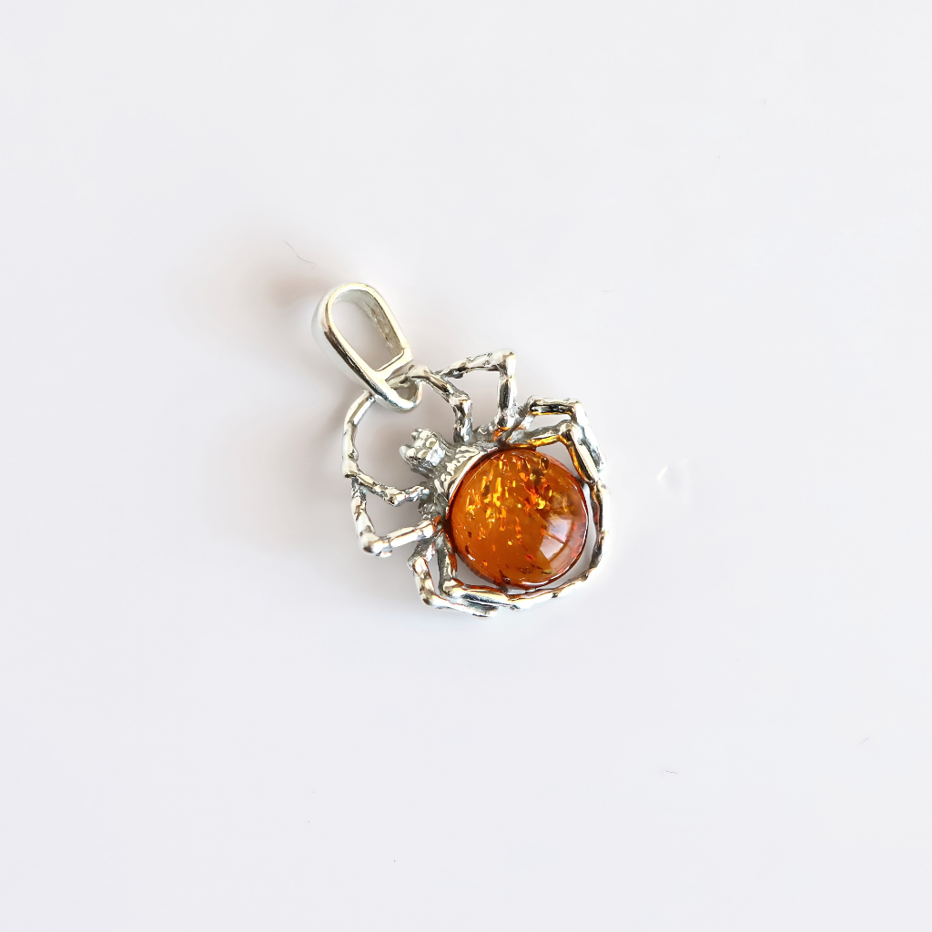 A amber spider-shaped silver pendant featuring a round amber-colored gemstone in the center, shown on a plain white background.