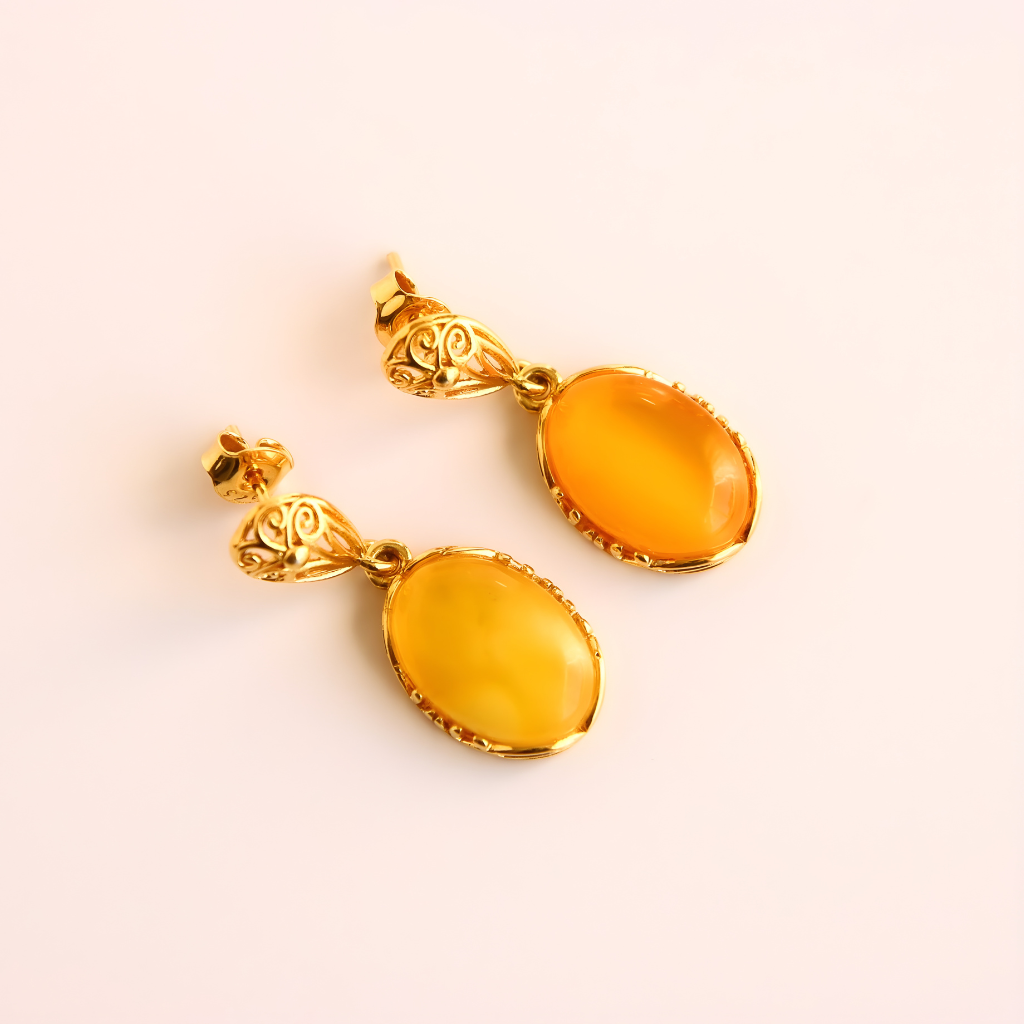 Gold earrings with amber-colored stones on a light pink background