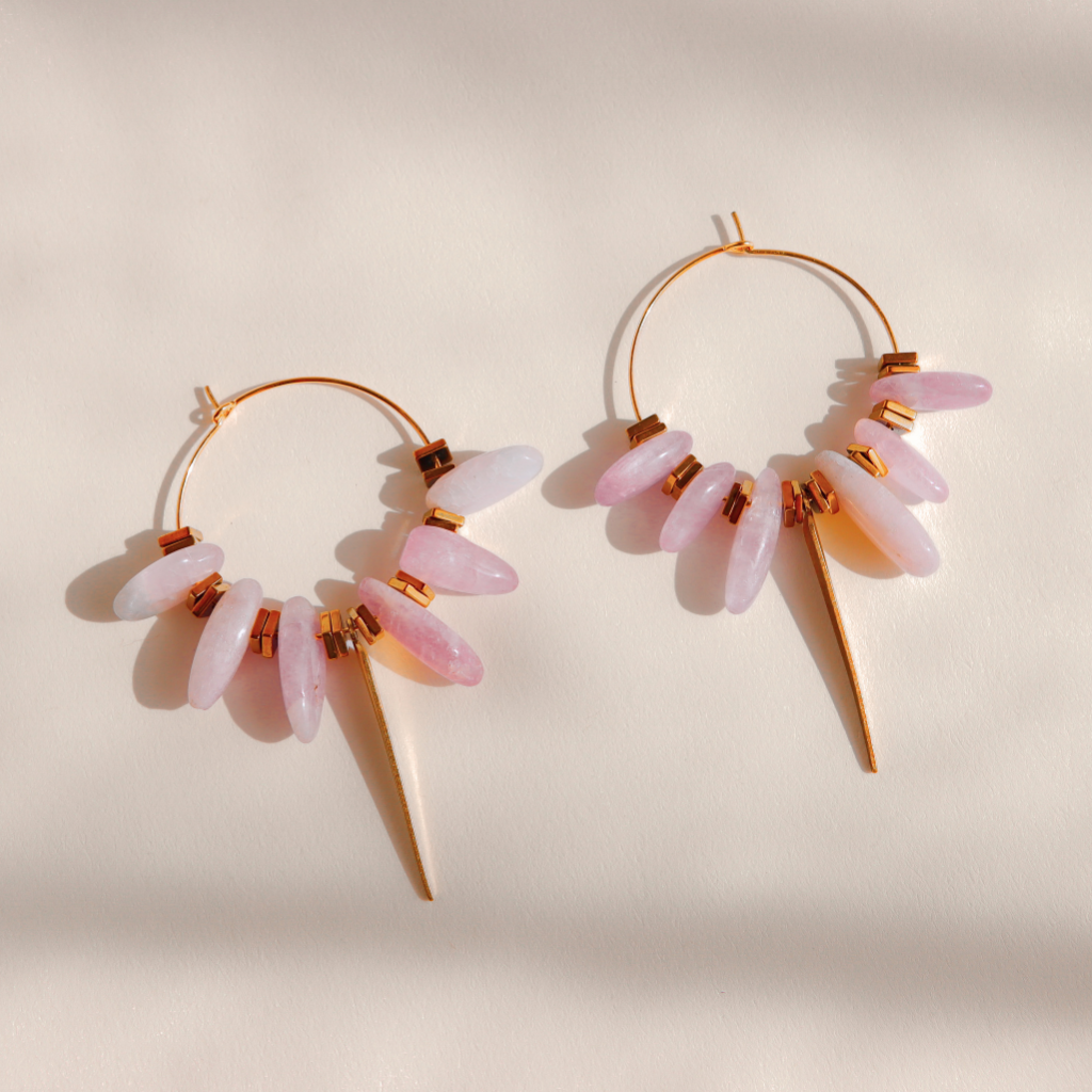 A pair of gold Kunzite hoop earrings with dangling pink and white stone clusters and pointed gold spikes, photographed on a warm off-white background with soft shadows.
