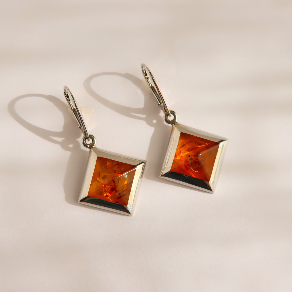 A pair of silver drop amber earrings with square amber gemstones, displayed on a clean white background with soft shadows.