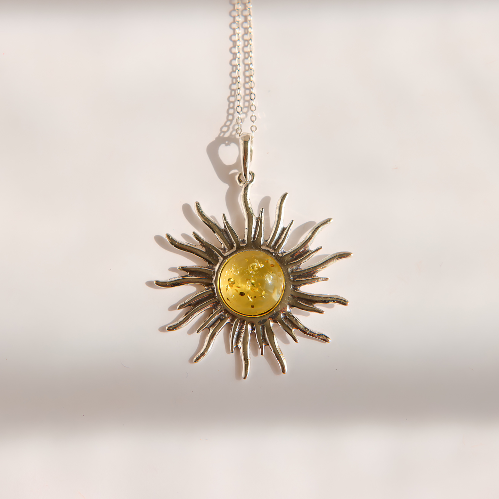 A silver lemon Baltic amber sun pendant necklace featuring a central round yellow amber inlay, suspended from a delicate silver chain against a warm off-white background.