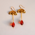 A pair of gold and red drop vintage lucite earrings on a light gray background. Each earring features a textured gold semi-circle top, a gold chain, and a faceted red teardrop bead.