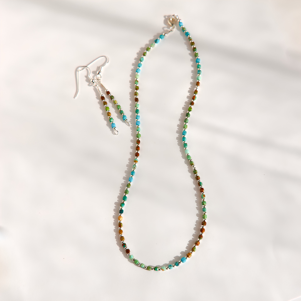 A beaded necklace and matching drop earrings laid out on a white fabric background. The jewelry features small multicolored Hubei turquoise beads with turquoise blue, green, and brown tones, suspended from silver-toned hooks.