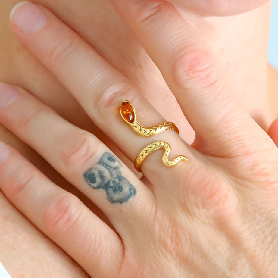 Gold snake ring on a finger with a tattoo of a bear.