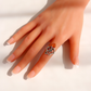 A silver amber octopus ring with a large amber stone  and a small amber-orange gemstone, worn on a hand with a French manicure against a bright white background.