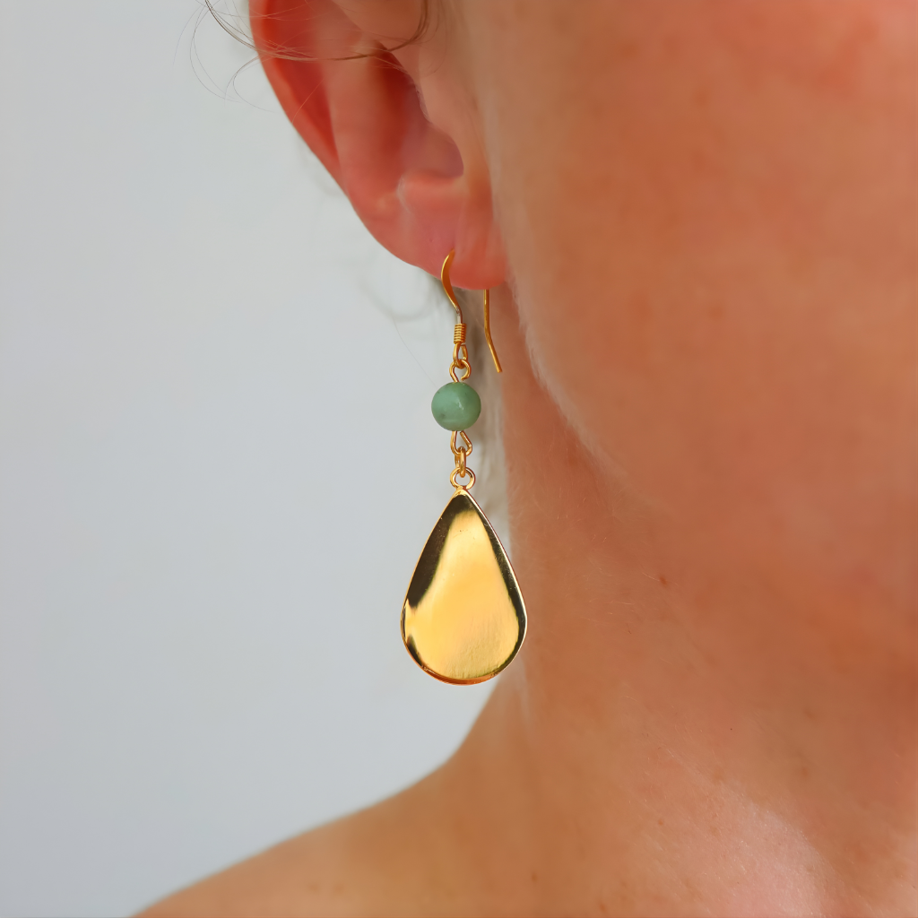 Gold drop earring with green gemstone on a neutral background