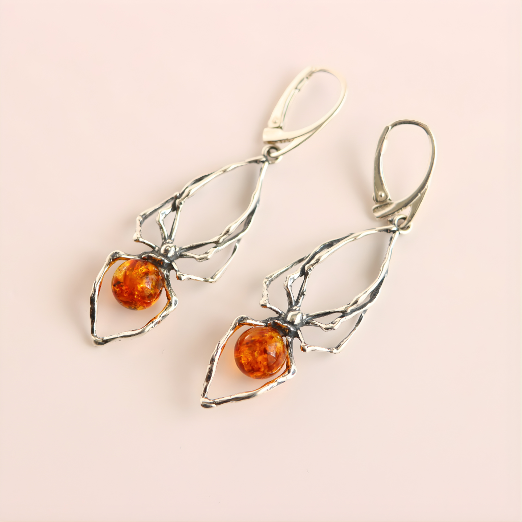 Silver spider earrings with amber stones on a light pink background